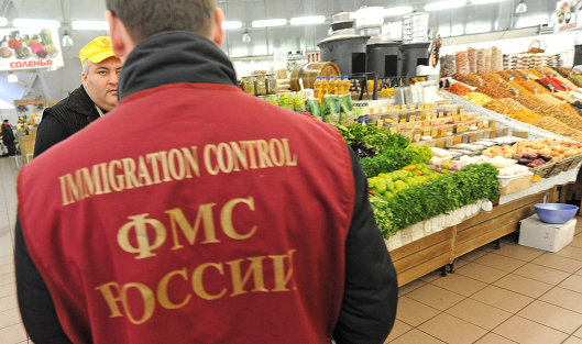 Сотрудник Федеральной миграционной службы РФ проверяет документы у торговца рынка 