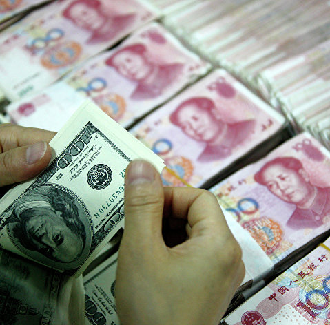 Банковский служащий пересчитывает доллары рядом с пачками юаней