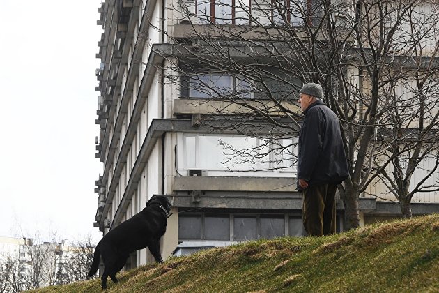 Мужчина выгуливает собаку рядом с жилым домом