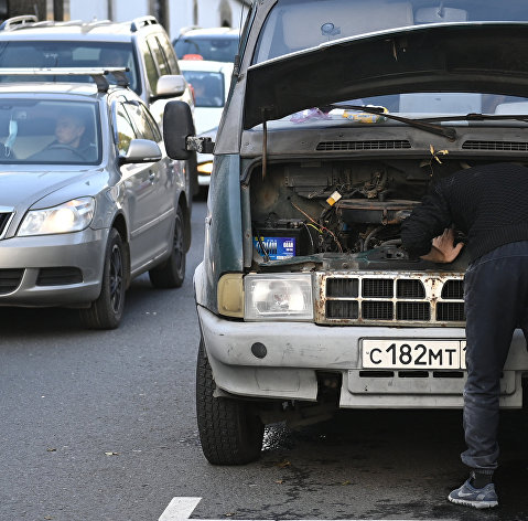 Мужчина пытается починить машину на дороге