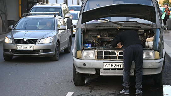 Мужчина пытается починить машину на дороге