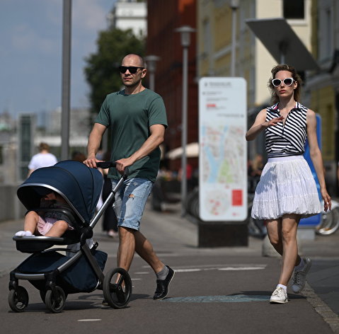 Жители Москвы гуляют с ребенком в коляске по набережной