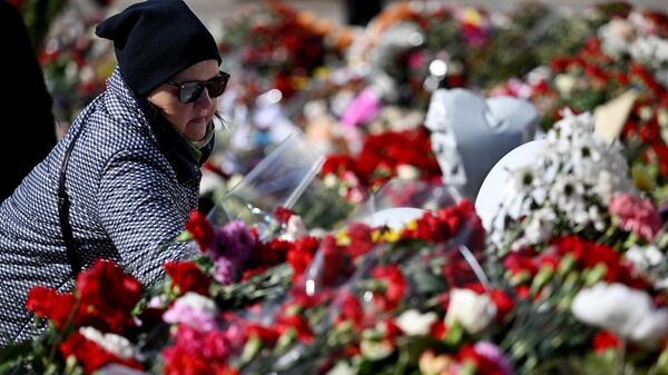 Женщина возлагает цветы к стихийному мемориалу возле подмосковного Крокус Сити Холла