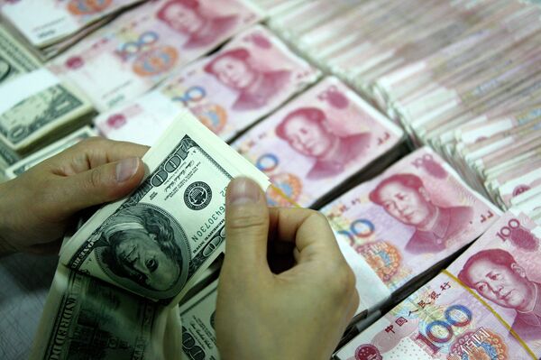 %Банковский служащий пересчитывает доллары рядом с пачками юаней