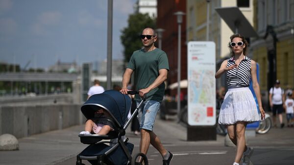 Жители Москвы гуляют с ребенком в коляске по набережной